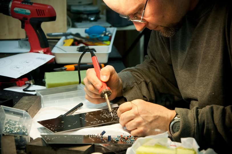 Mężczyzna lutujący elementy elektroniczne na płytce drukowanej w warsztacie